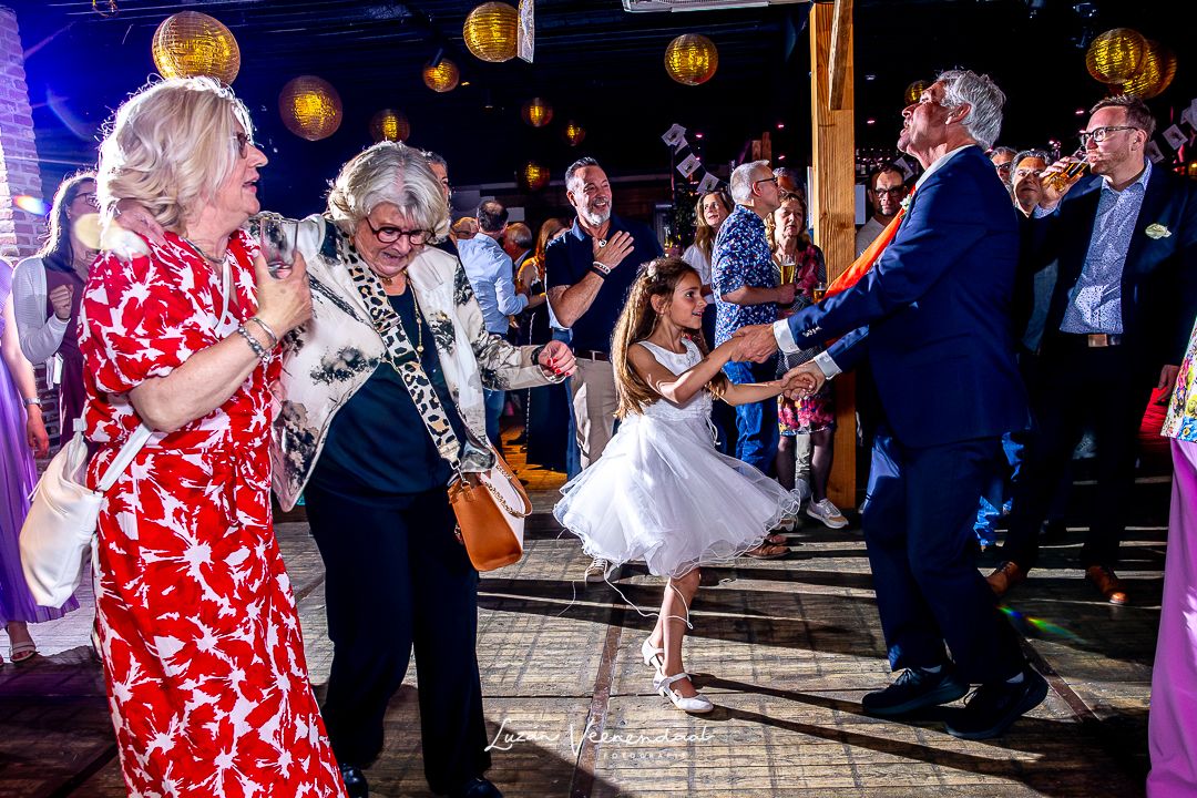 Vader van de bruid danst op de dansvloer met het bruidsmeisje en beide moeders tijdens het feest
