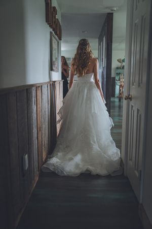 Bride in a flowing white ballgown wedding dress standing in a hallway, viewed from behind.