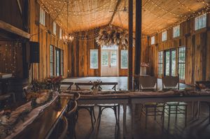 Rustic barn wedding reception venue with string lights, wooden walls, and elegant farm tables with chairs.