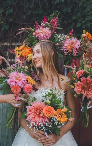 Smiling bride in white dress holds colorful bouquet surrounded by vibrant pink and orange floral arrangements.