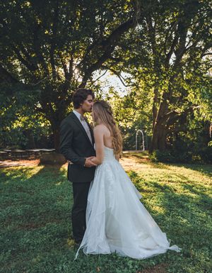 Bride and groom share romantic moment in sunlit garden, bride wearing flowing white ball gown.