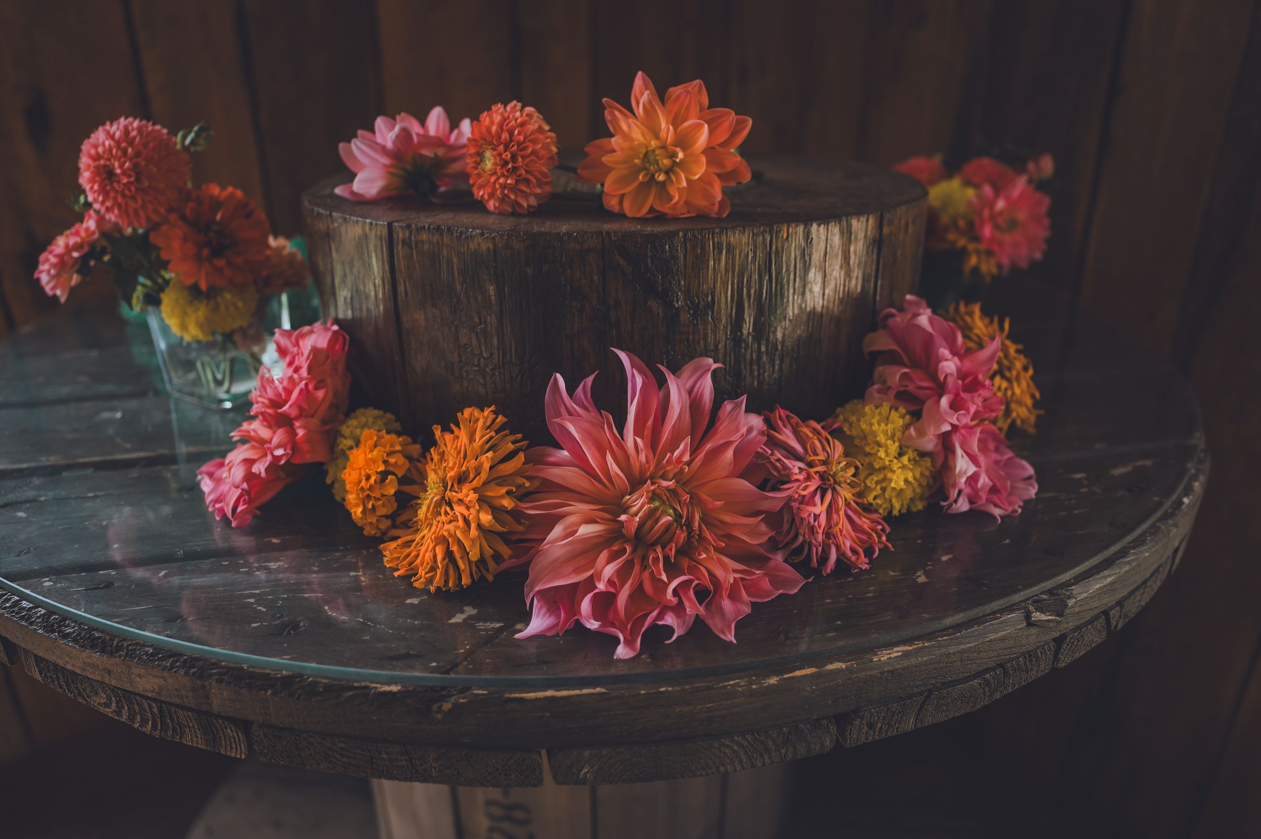 Rustic wedding decor with pink and orange dahlias arranged around wooden log centerpiece on barrel table.