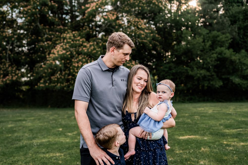 Happy young family with two small children sharing a tender moment together in a green outdoor setting.