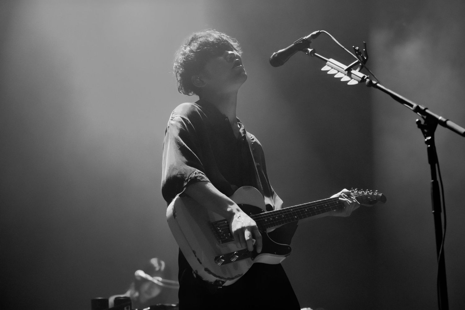 A black and white concert photo of TK from Ling Tosite Sigure singing into the mic while holding a guitar at the Belasco in LA.
