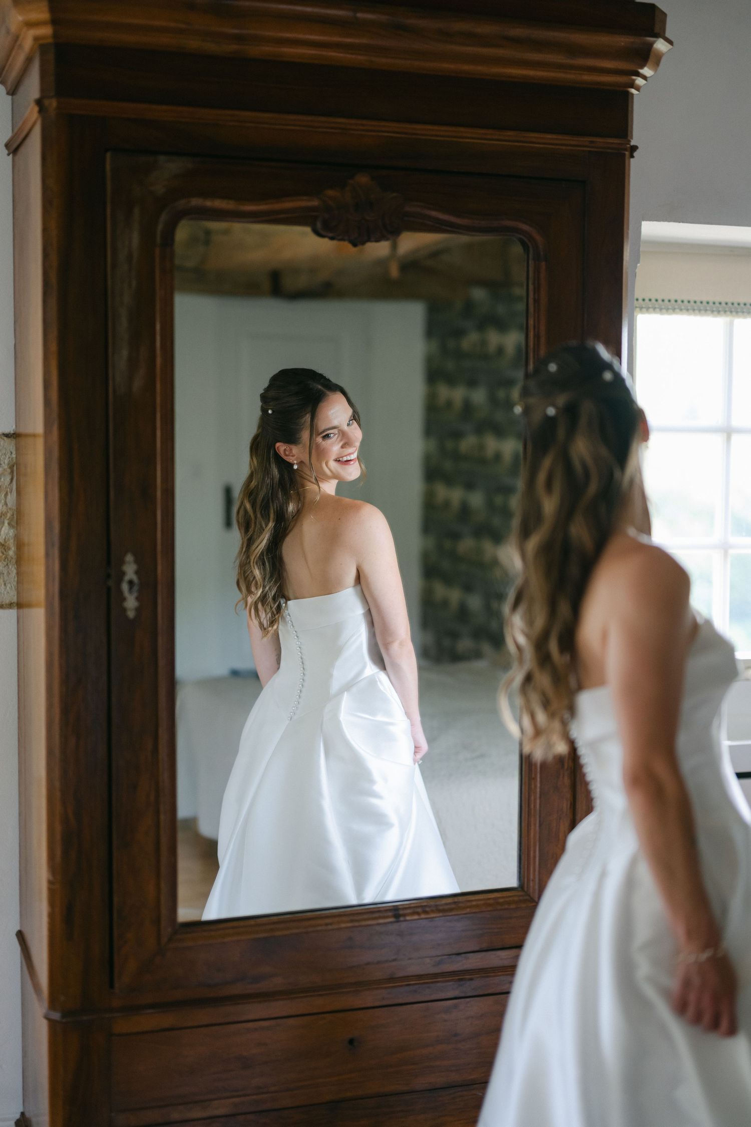 Smiling bride in strapless white gown posing on wooden staircase in elegant interior setting.