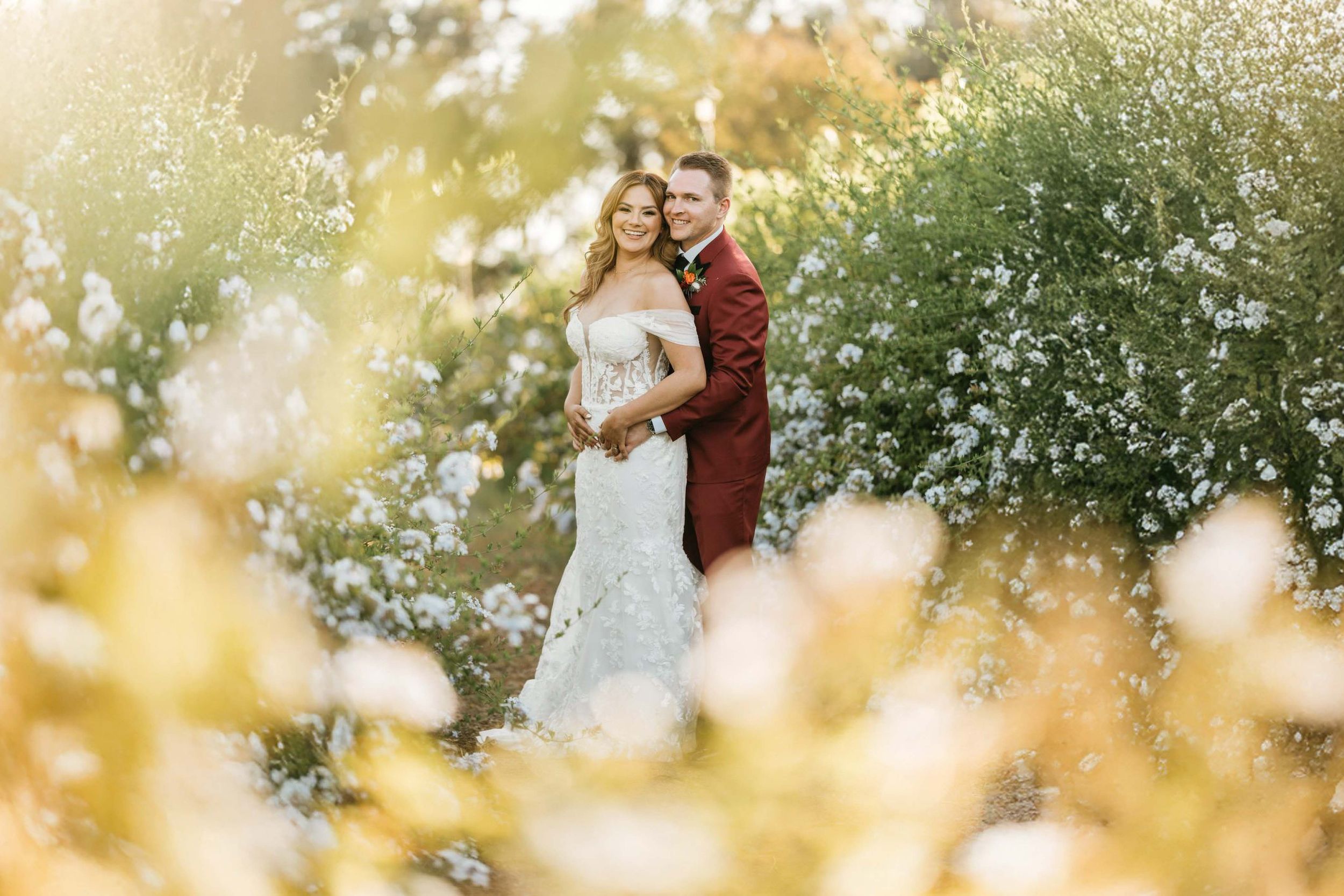 Bride and groom embracing among blooming white flowers during golden hour portraits at Lake Oak Meadows in Temecula, California.