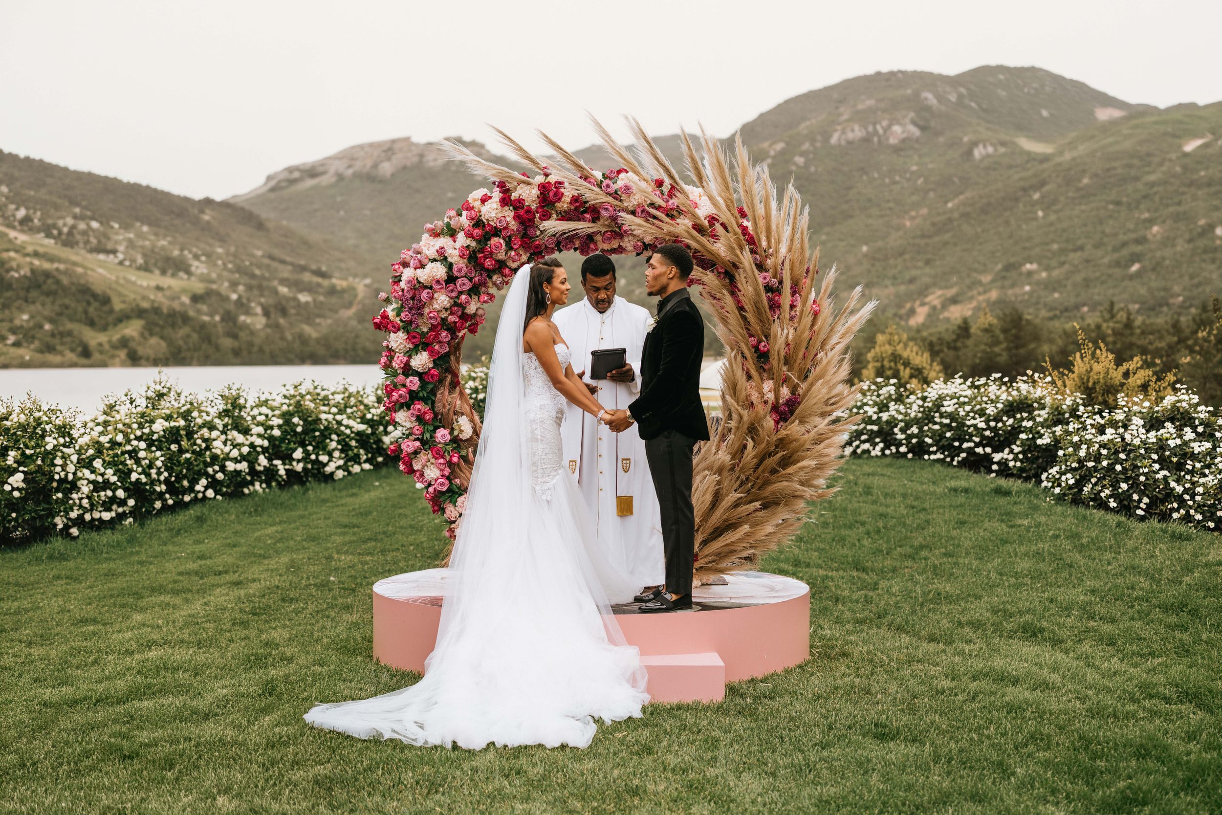 Bride and groom exchanging vows beneath a floral ceremony arch overlooking the lake at Epona Estate in Hidden Valley, California.