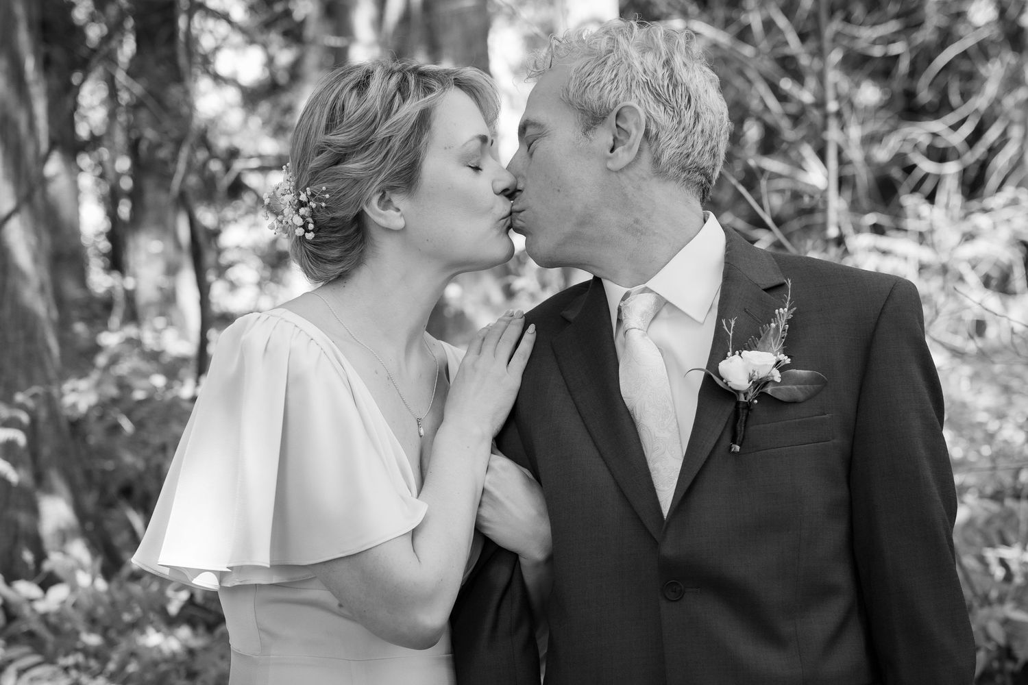 Black and white photo of a bride and groom sharing a romantic kiss outdoors on their wedding day.