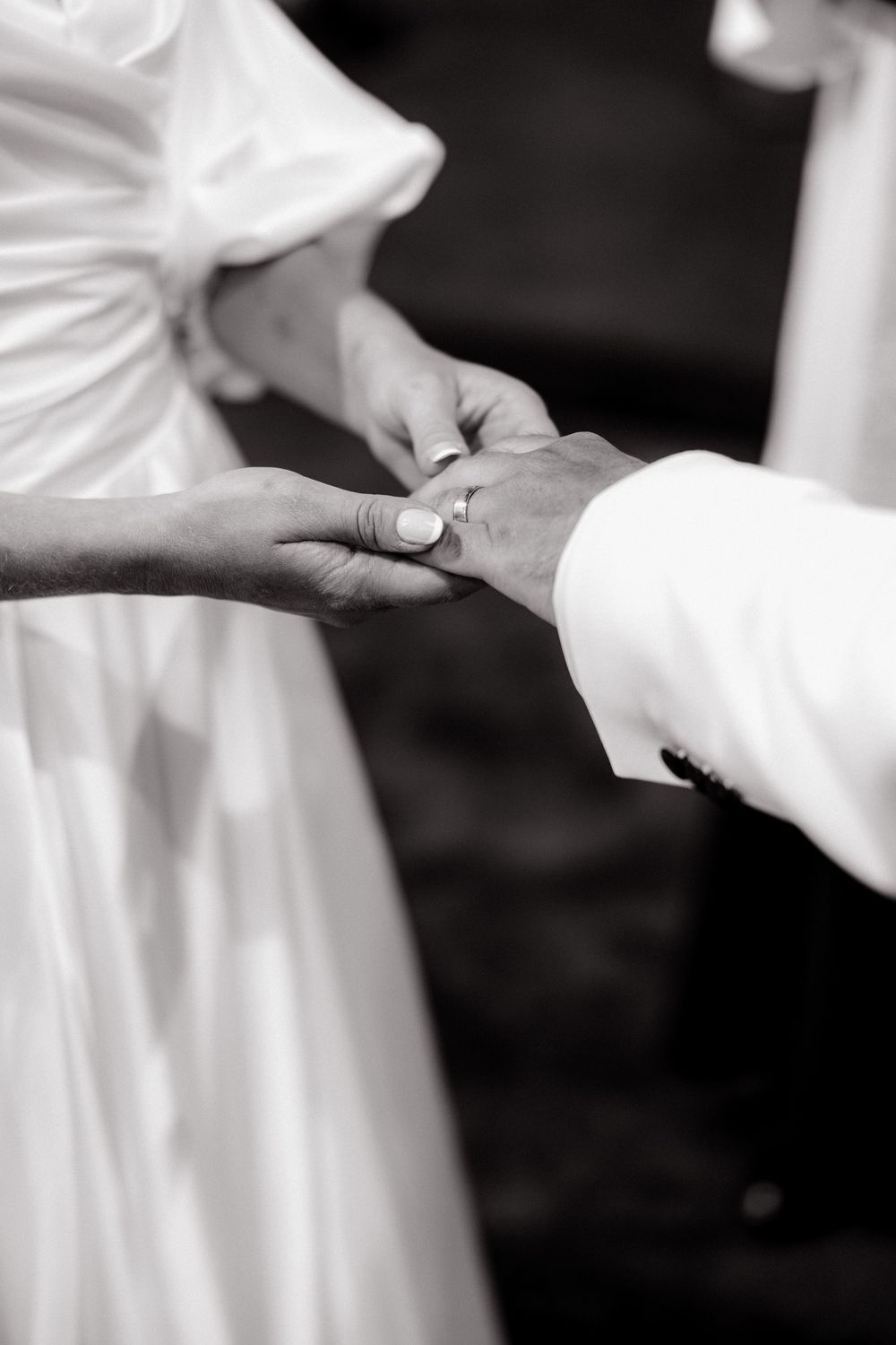 Black and white photo of bride and groom exchanging wedding rings during ceremony.
