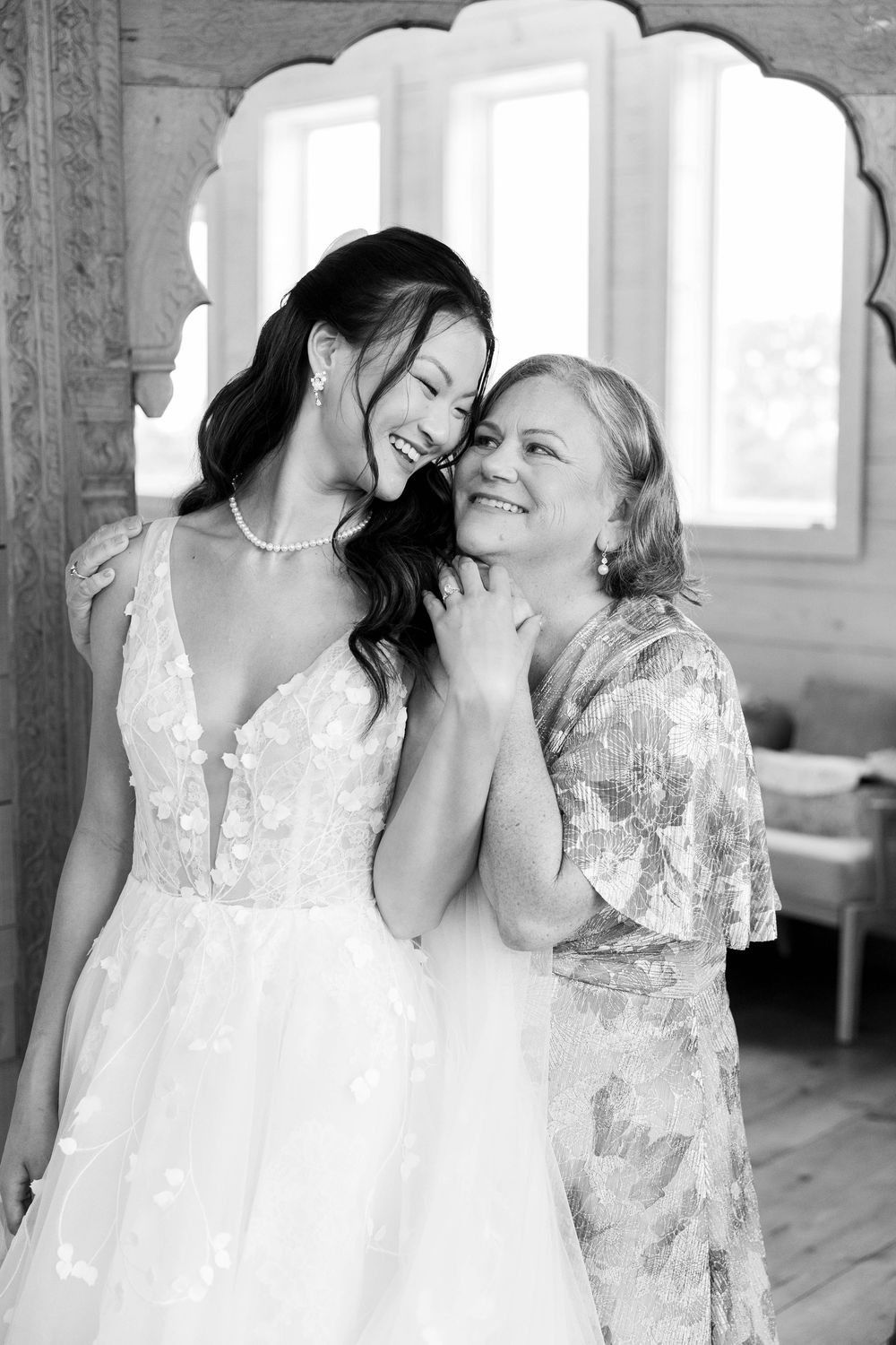 Black and white photo of a bride in lace gown sharing a joyful moment with an older woman indoors taken by Nicole Parker Photography