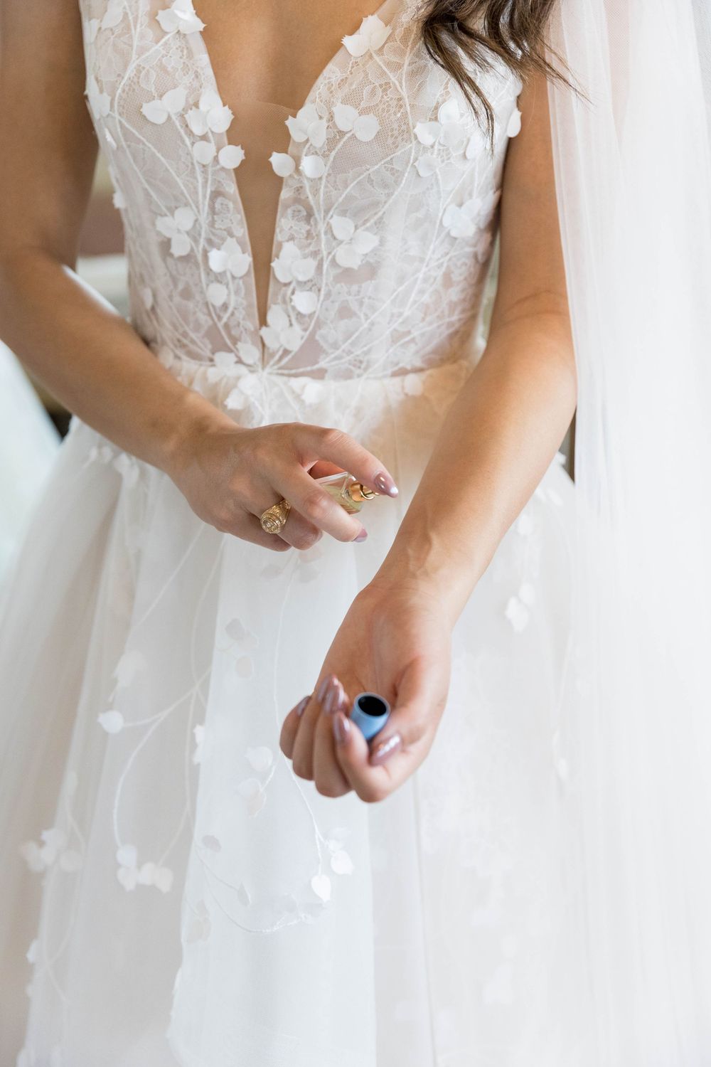 Bride in lace floral wedding gown holding rings, wearing a veil, with elegant manicured nails.