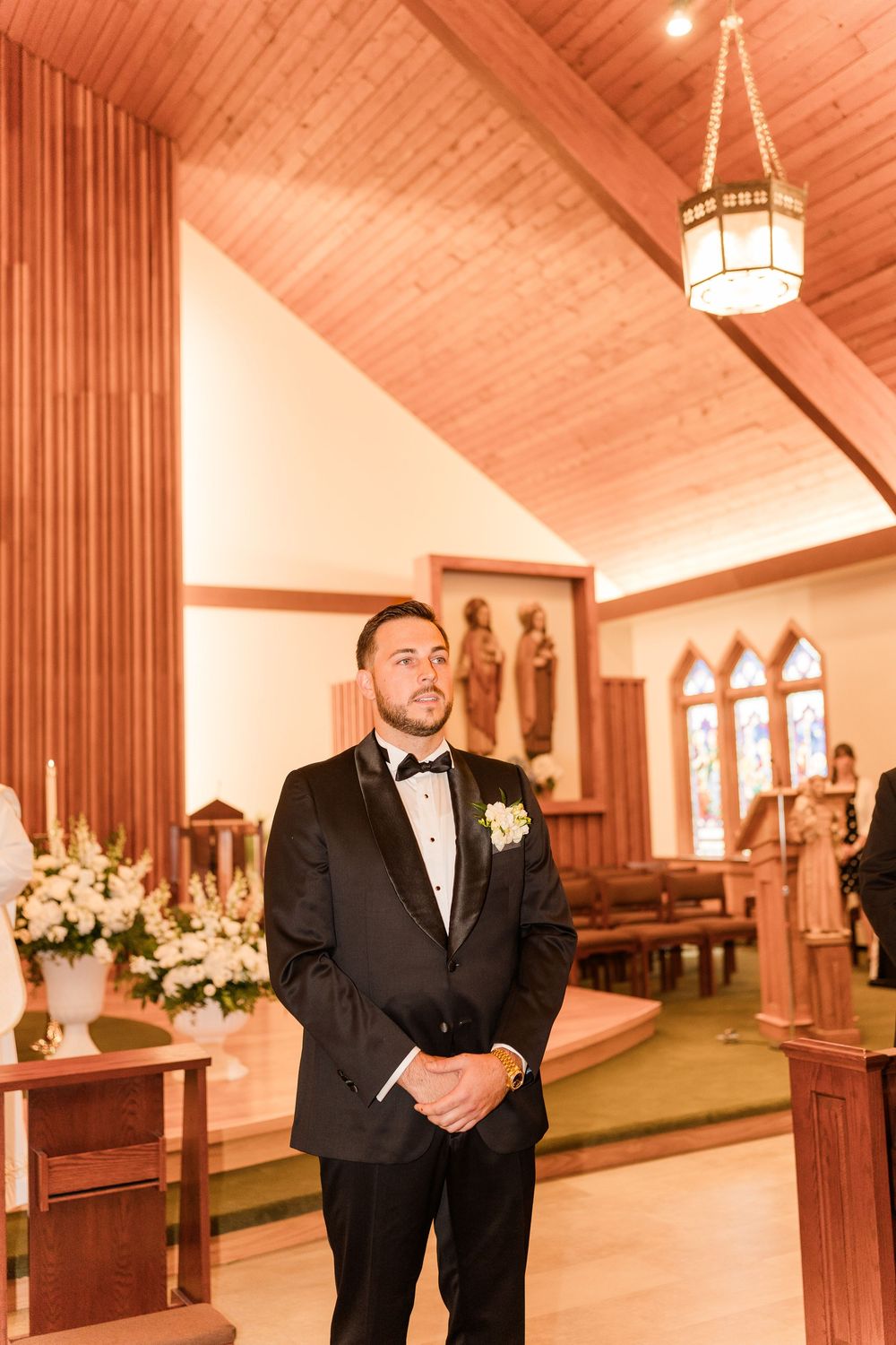 Groom in black tuxedo stands at church altar awaiting bride during wedding ceremony.