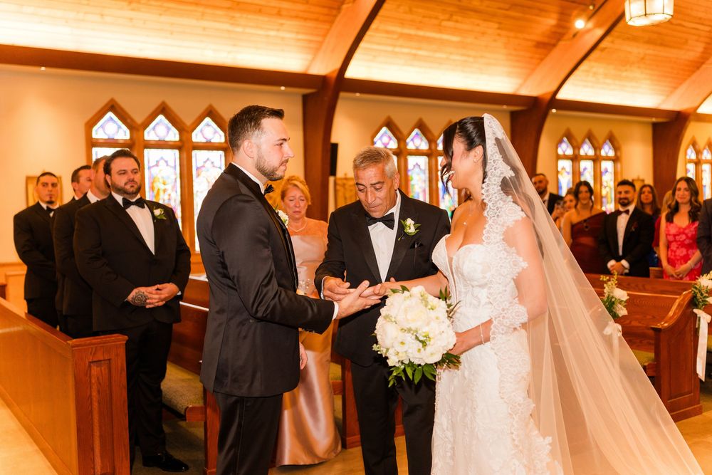 Bride and groom exchange rings at elegant chapel wedding ceremony with guests seated in wooden pews.