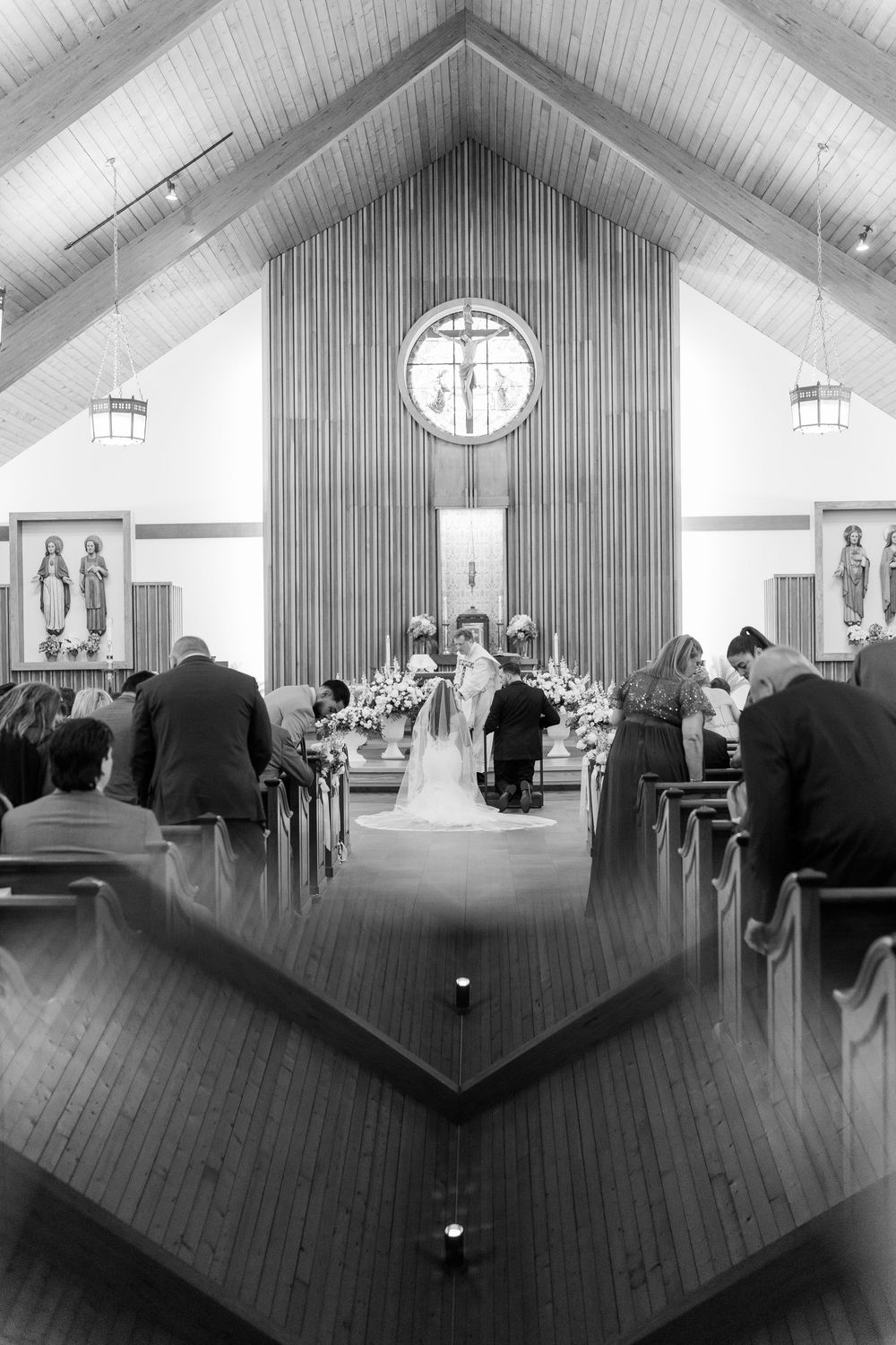 Black and white photo of a wedding ceremony inside a church with guests seated in pews.