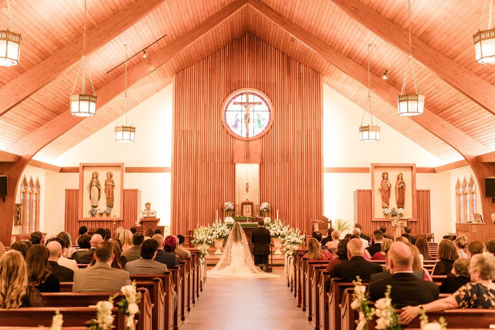 Elegant church wedding ceremony with wooden pews, floral arrangements, and a cross above the altar in a warm-lit chapel.