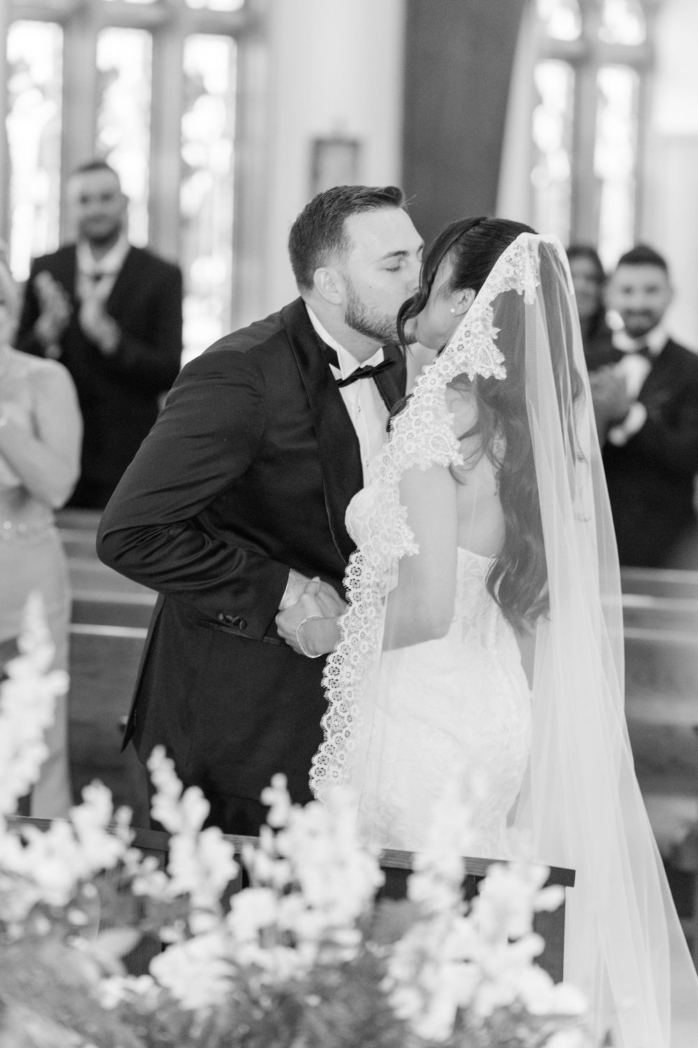 Black and white photo of a groom kissing his bride at the altar during a church wedding ceremony.