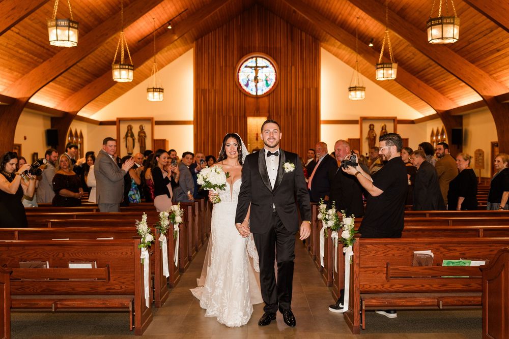 Newlyweds walk down the aisle as guests cheer in a wooden chapel after their wedding ceremony.