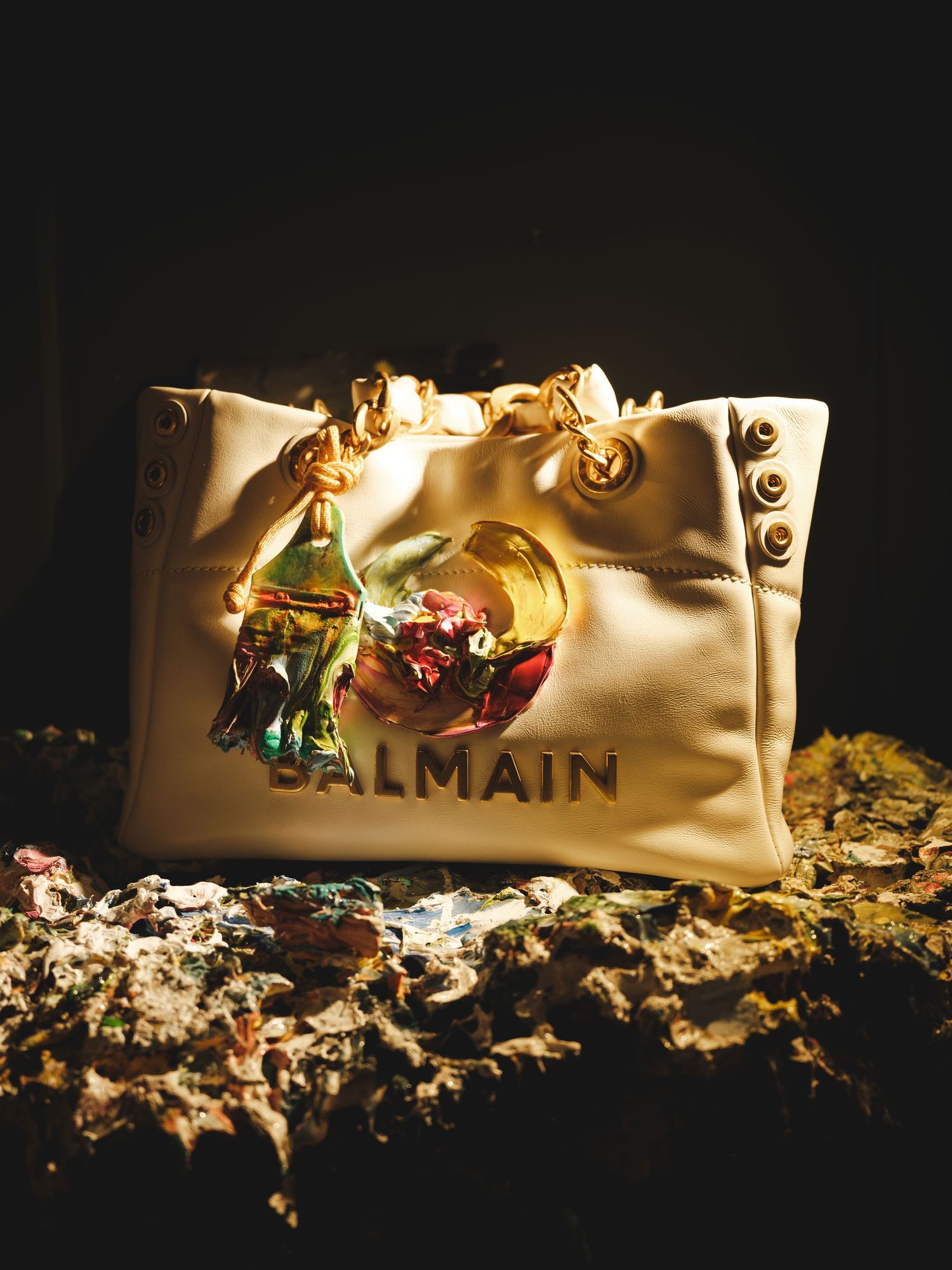 Balmain cream tote bag with gold hardware and colorful graphic print, displayed on a dark textured surface.