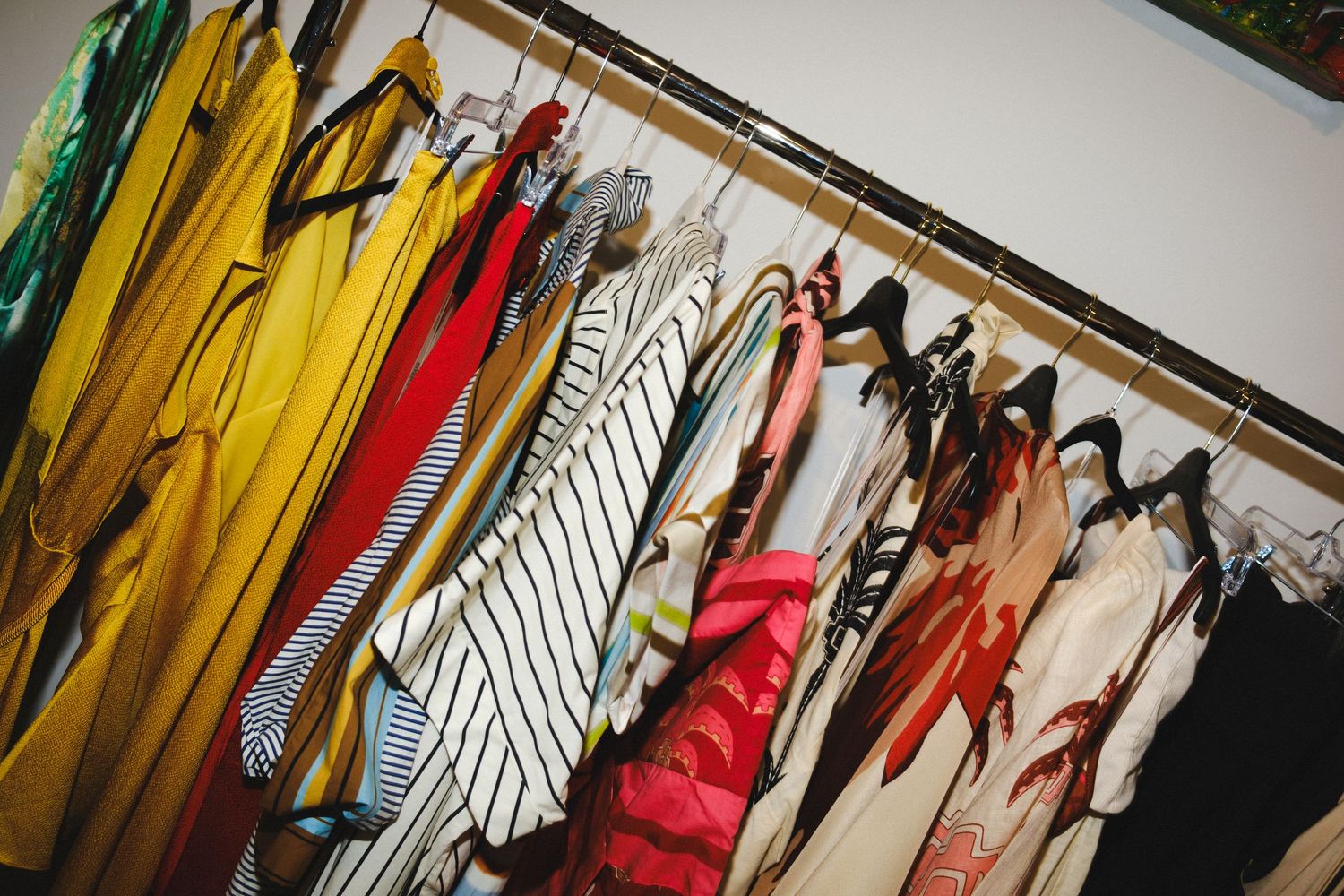 Colorful clothing items hanging on a wooden rack, featuring yellow, striped, red, and floral garments in a boutique.