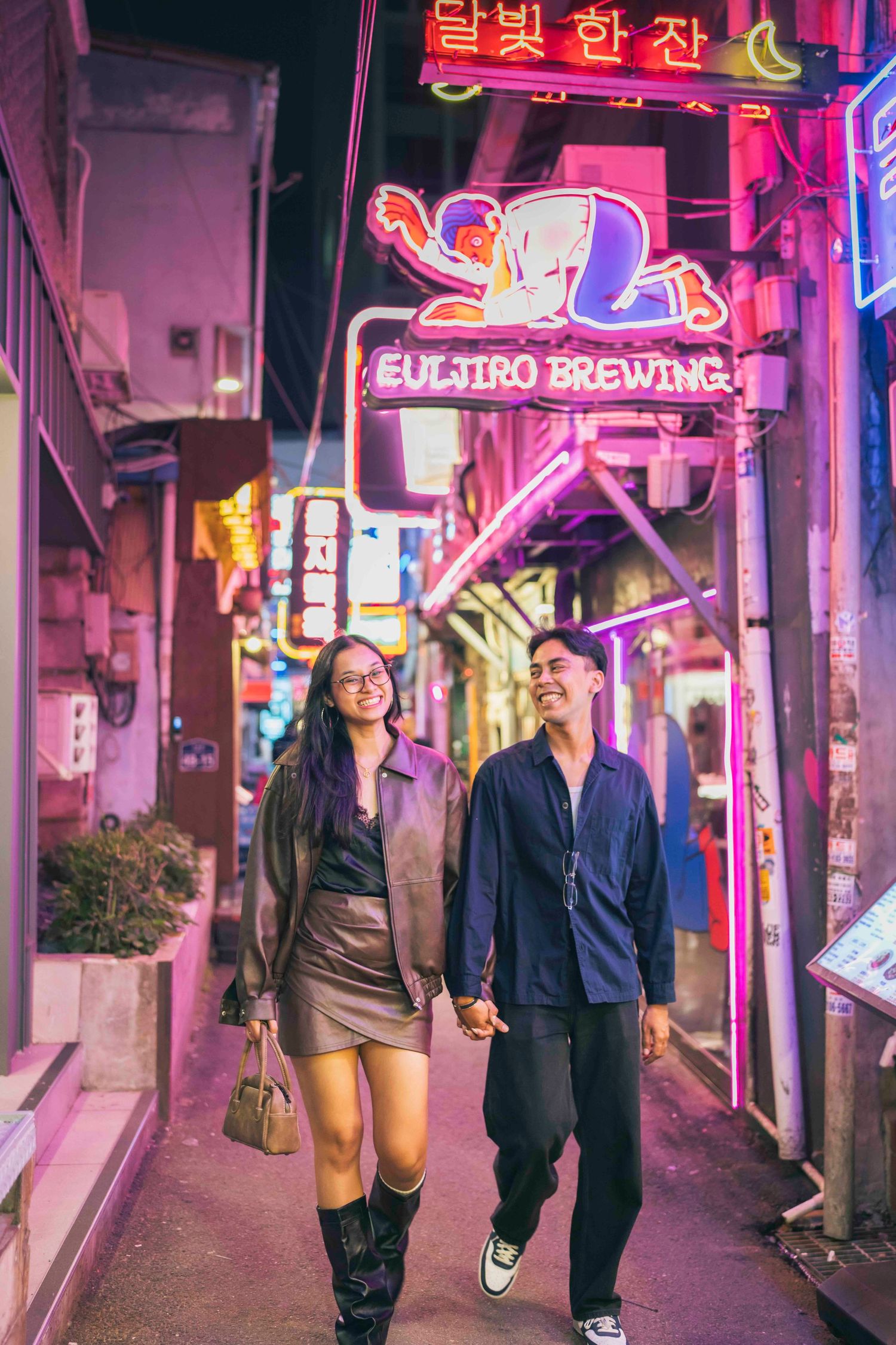 Couple holding hands walking through vibrant neon-lit alley near Euljiro Brewing in Seoul at night.