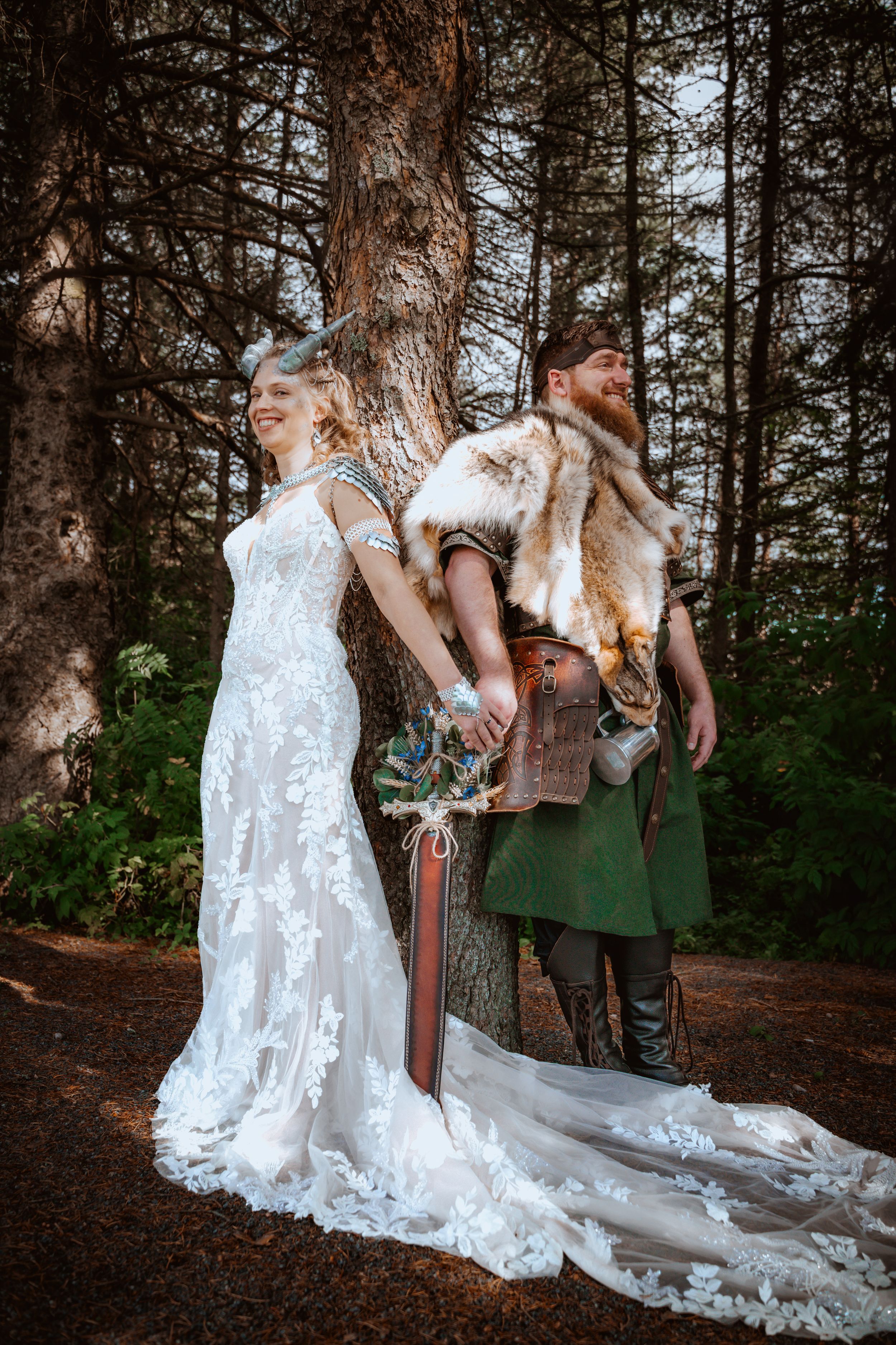 Mariés de style viking posant en forêt : robe de dentelle avec cornes et costume en fourrure avec une épée.