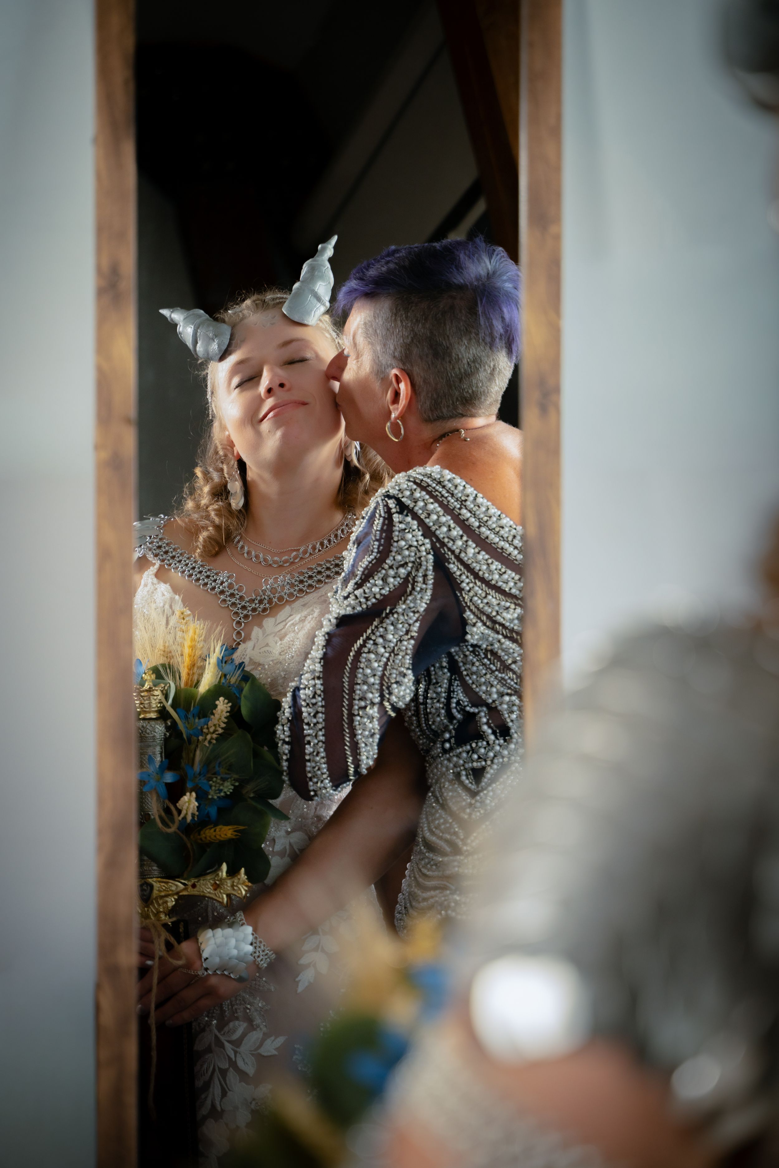 Reflet dans le miroir d'une mère embrassant la joue de sa fille, une mariée coiffée de cornes vikings.