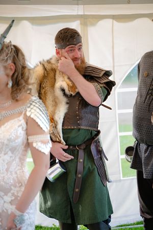 Le marié en costume de style viking et fourrure essuie une larme d'émotion durant la cérémonie.