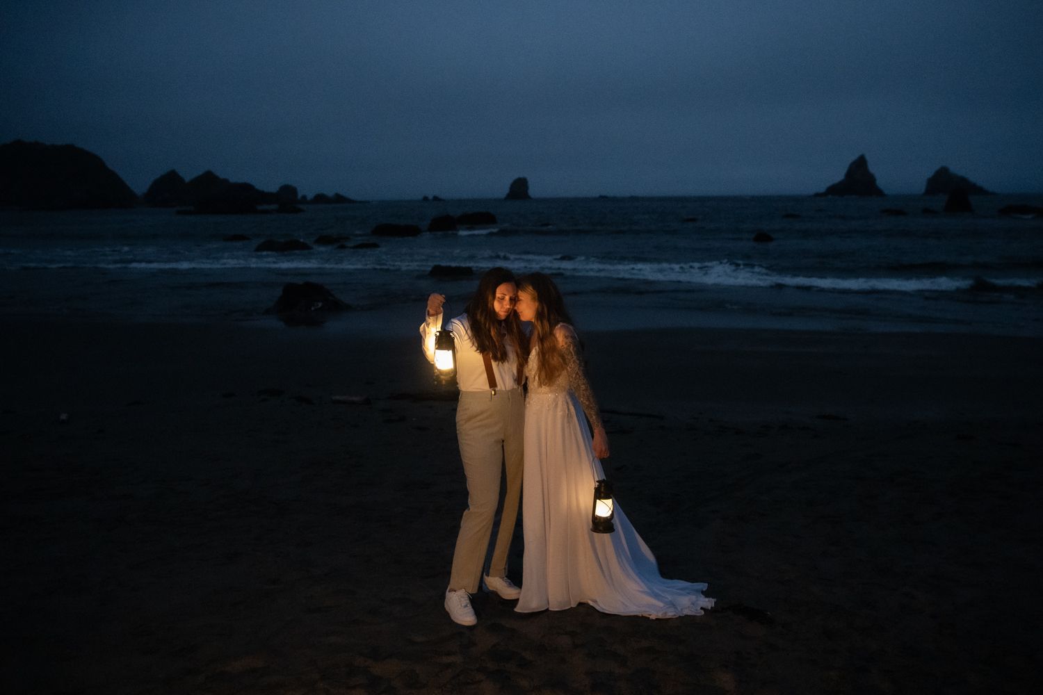 Two brides at blue hour holding lanterns on the Oregon coast