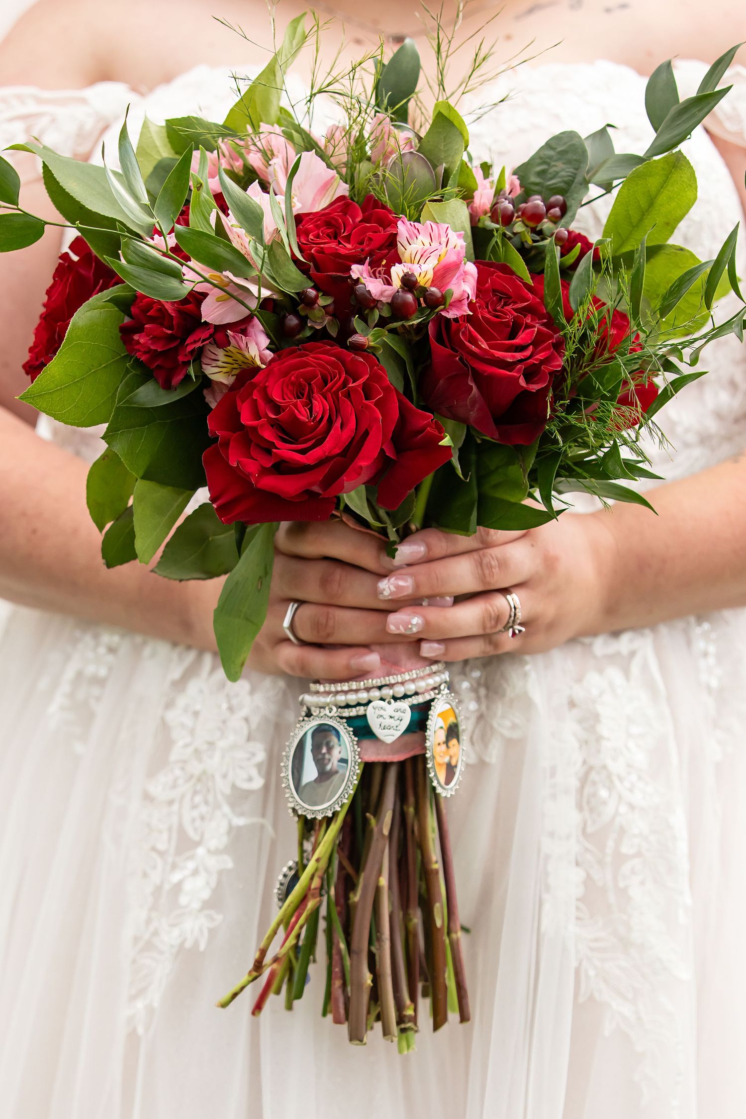 Bride and groom holding a lush pink and mauve bridal bouquet with greenery, bride in lace gown, groom in gray suit.