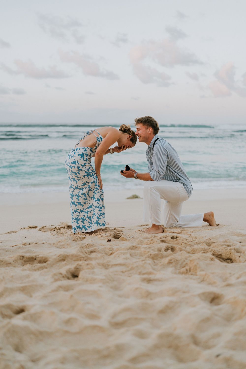 Couple celebrating engagement at Melasti Beach with ocean backdrop.