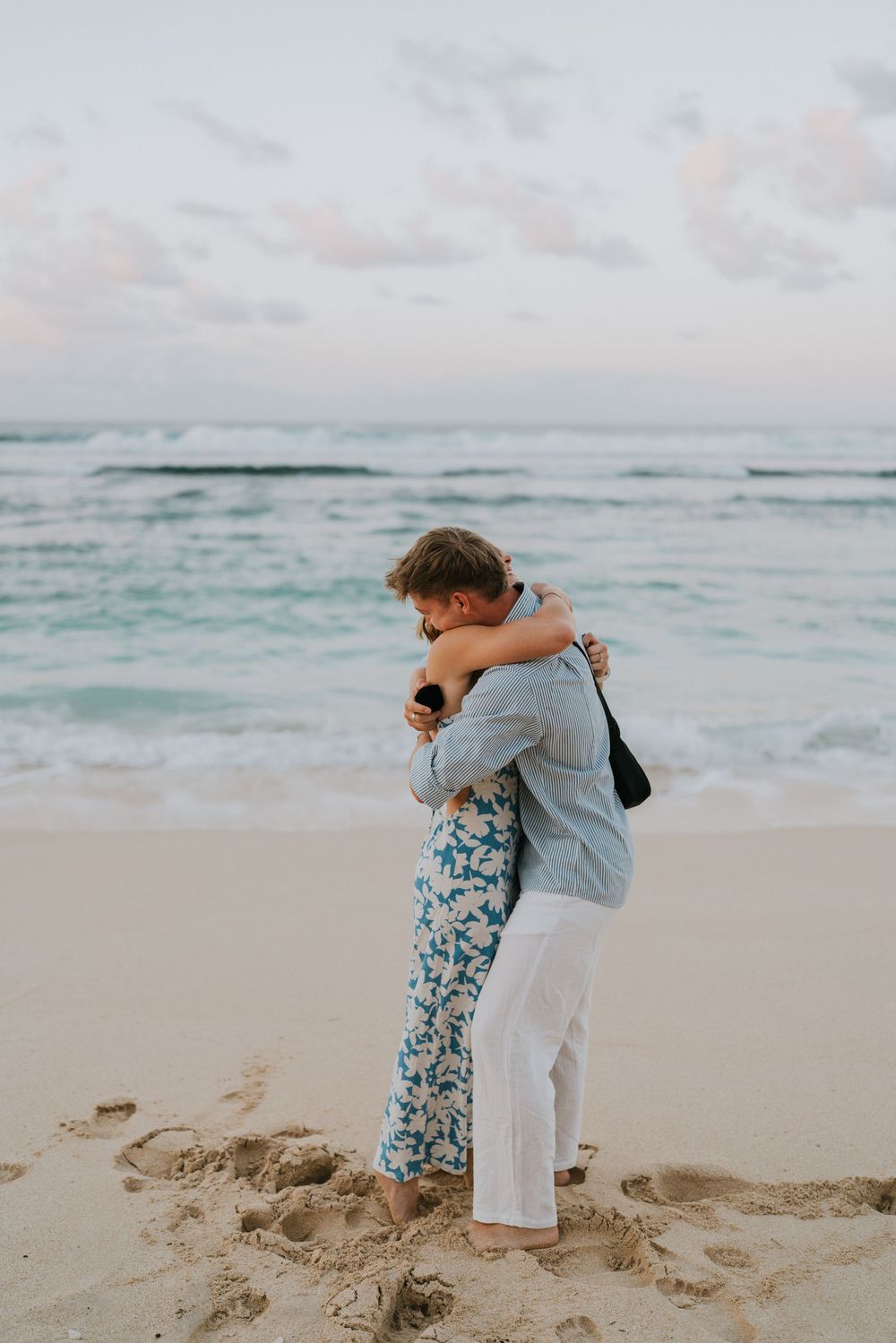 Couple celebrating engagement at Melasti Beach with ocean backdrop.