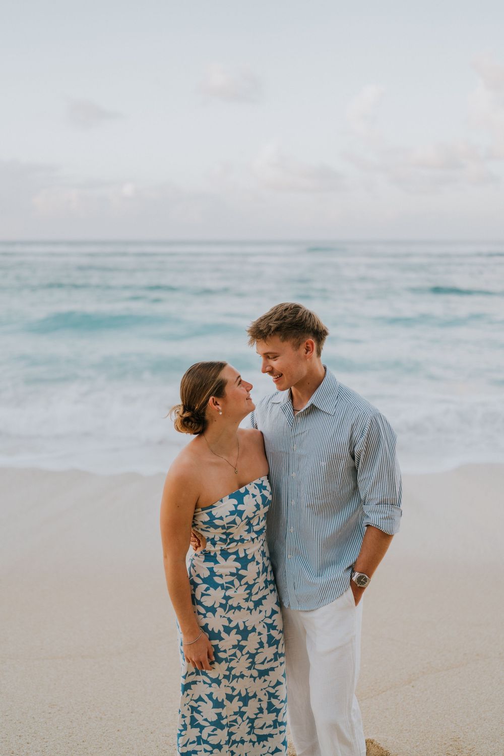 Couple celebrating engagement at Melasti Beach with ocean backdrop.