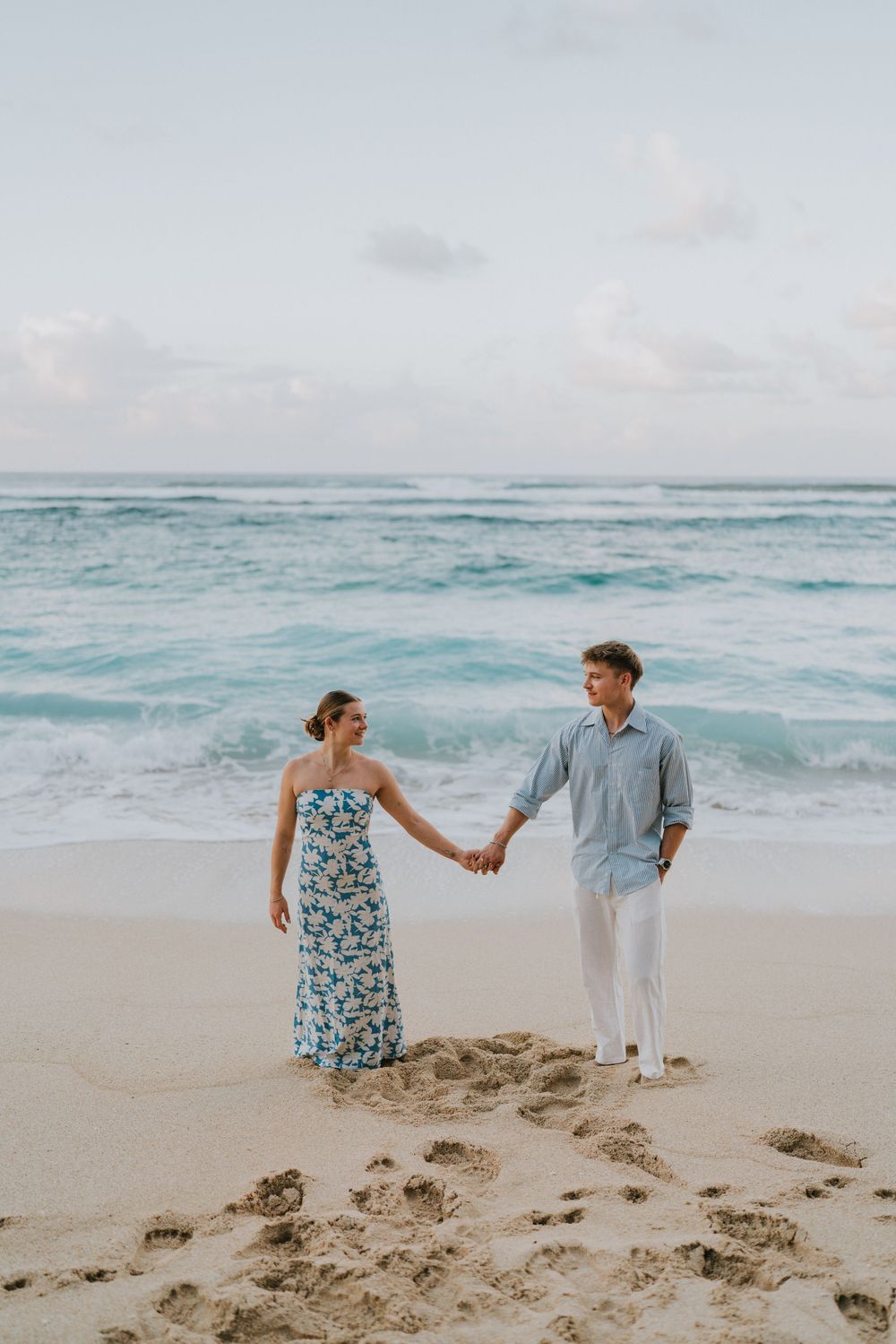 Couple celebrating engagement at Melasti Beach with ocean backdrop.