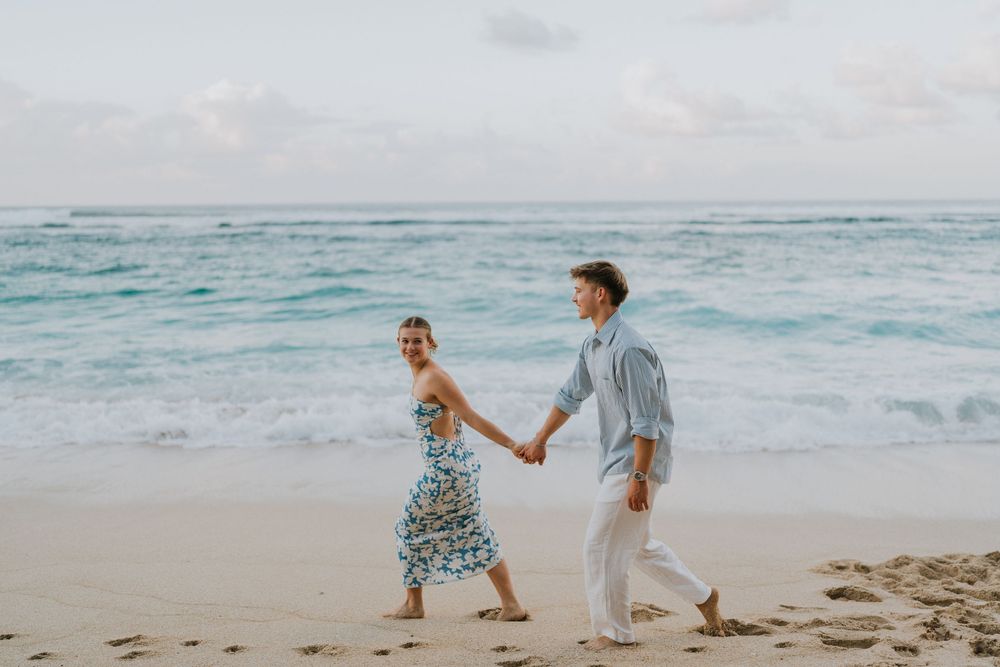 Couple celebrating engagement at Melasti Beach with ocean backdrop.