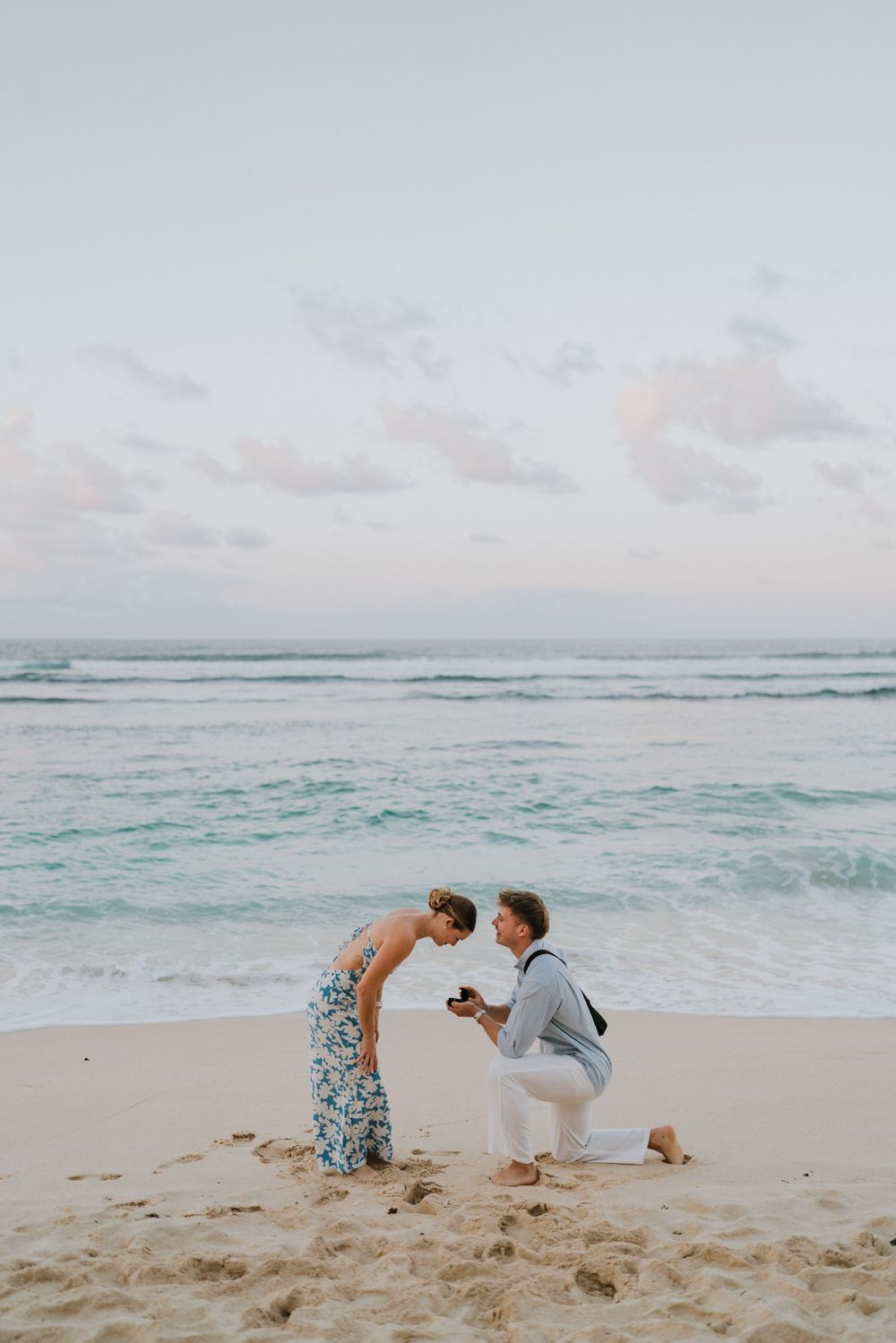 Couple celebrating engagement at Melasti Beach with ocean backdrop.