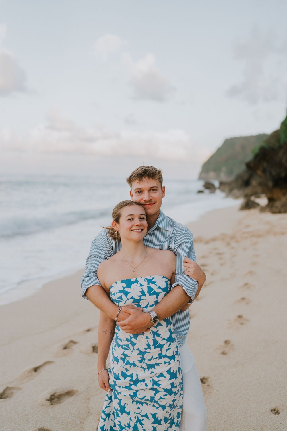 Couple celebrating engagement at Melasti Beach with ocean backdrop.
