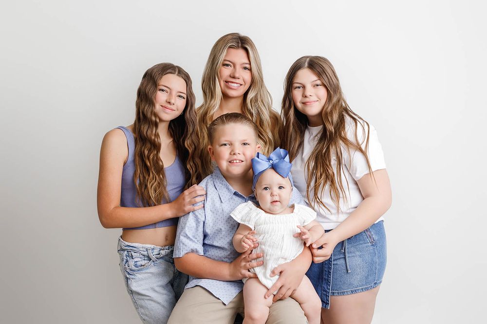 A smiling mother poses with her four young children in a bright studio portrait session.