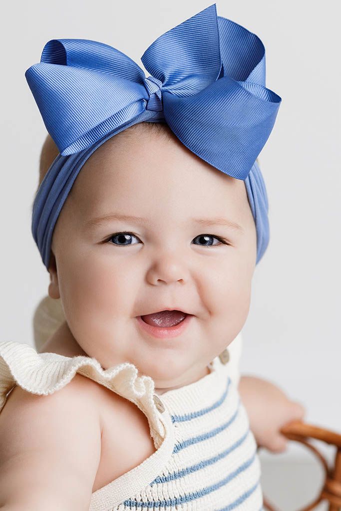 Close-up portrait of a smiling baby wearing a large blue bow headband and striped outfit.