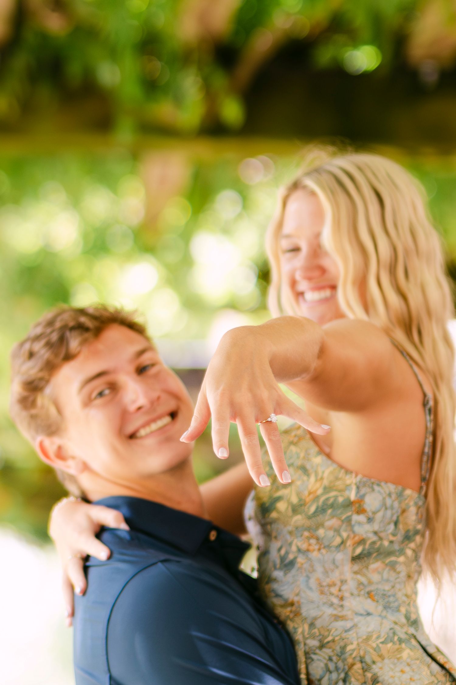 Happy couple showing off engagement ring outdoors.