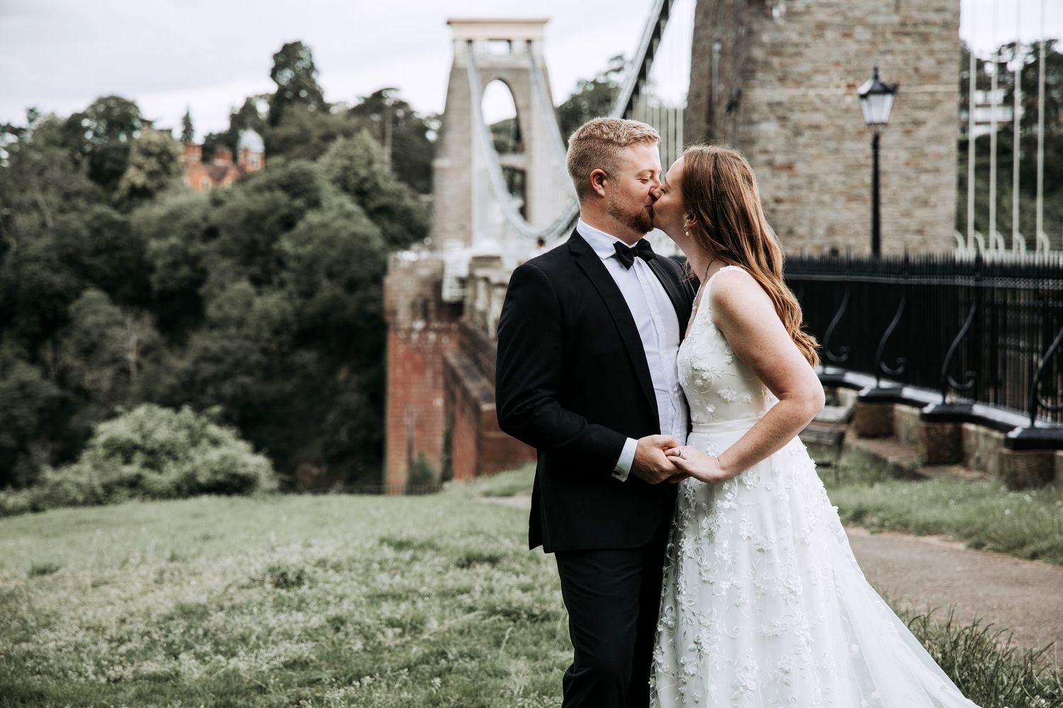 Bride and groom sharing a kiss beside Clifton Suspension Bridge after their Bristol wedding.