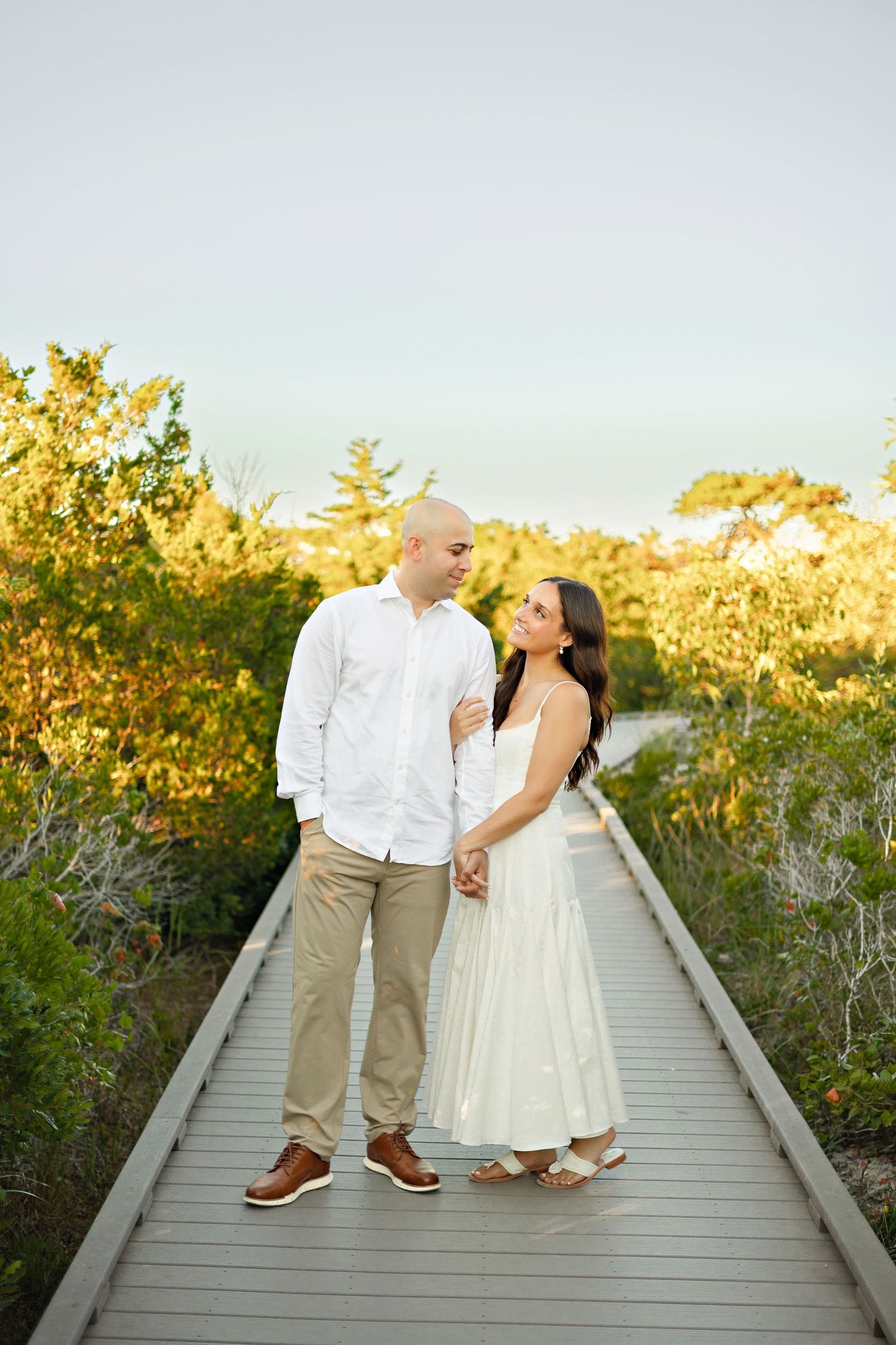 A couple embraces lovingly on a dirt path beside tall ornamental grasses on an overcast afternoon.