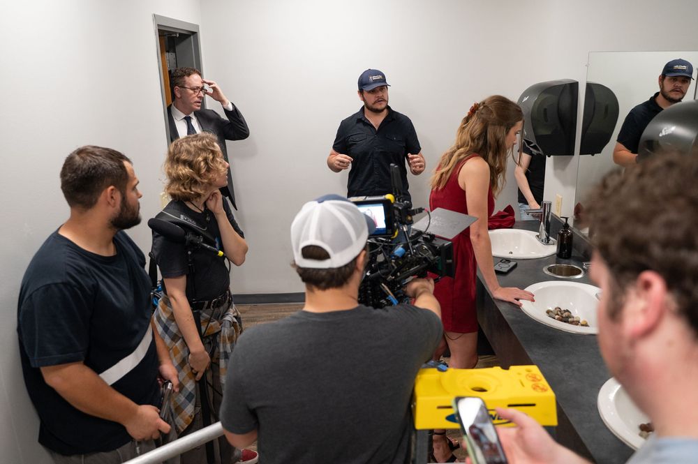 Film crew gathered in a room during a movie production shoot, with camera equipment and director giving instructions.