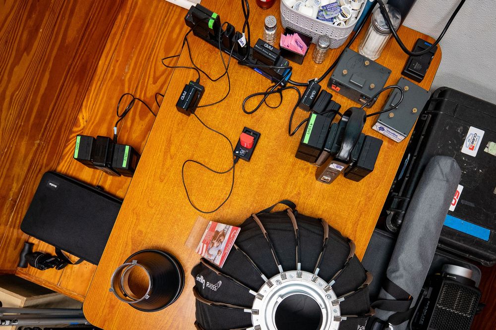 Overhead view of a wooden desk with cameras, electronics, cables, and equipment scattered across the surface.