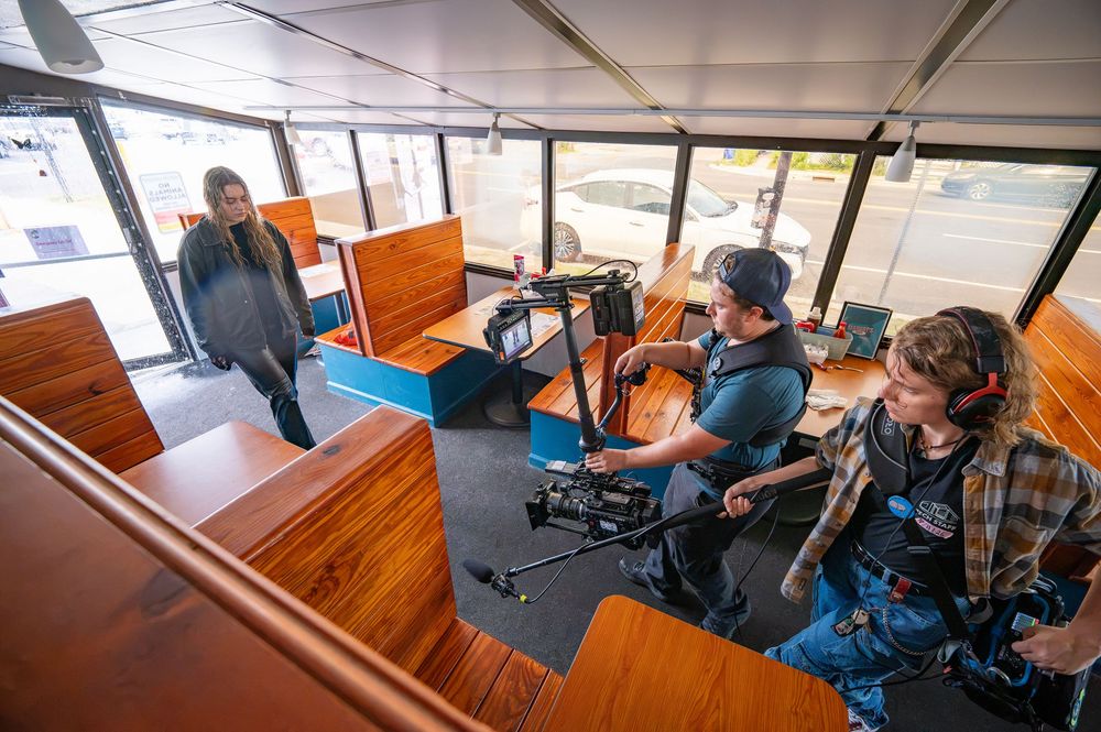 Film crew operating camera equipment inside a wooden trolley car during a video production shoot.