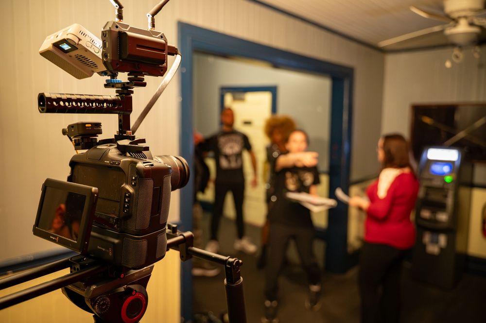 A professional camera on a stabilizer rig films actors in a doorway during an indoor video production shoot.