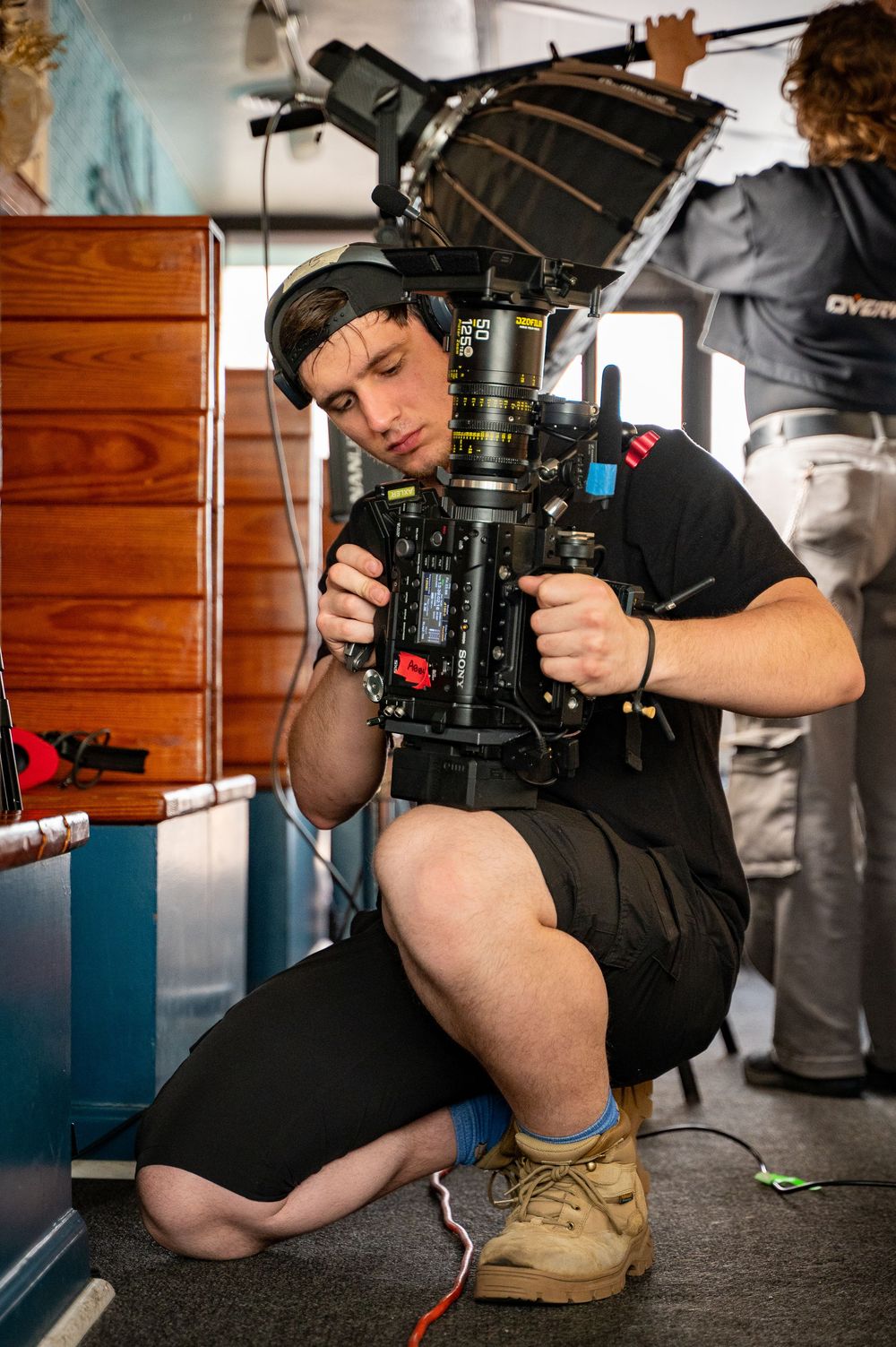 Cameraman crouching while operating a professional cinema camera on a film set indoors.