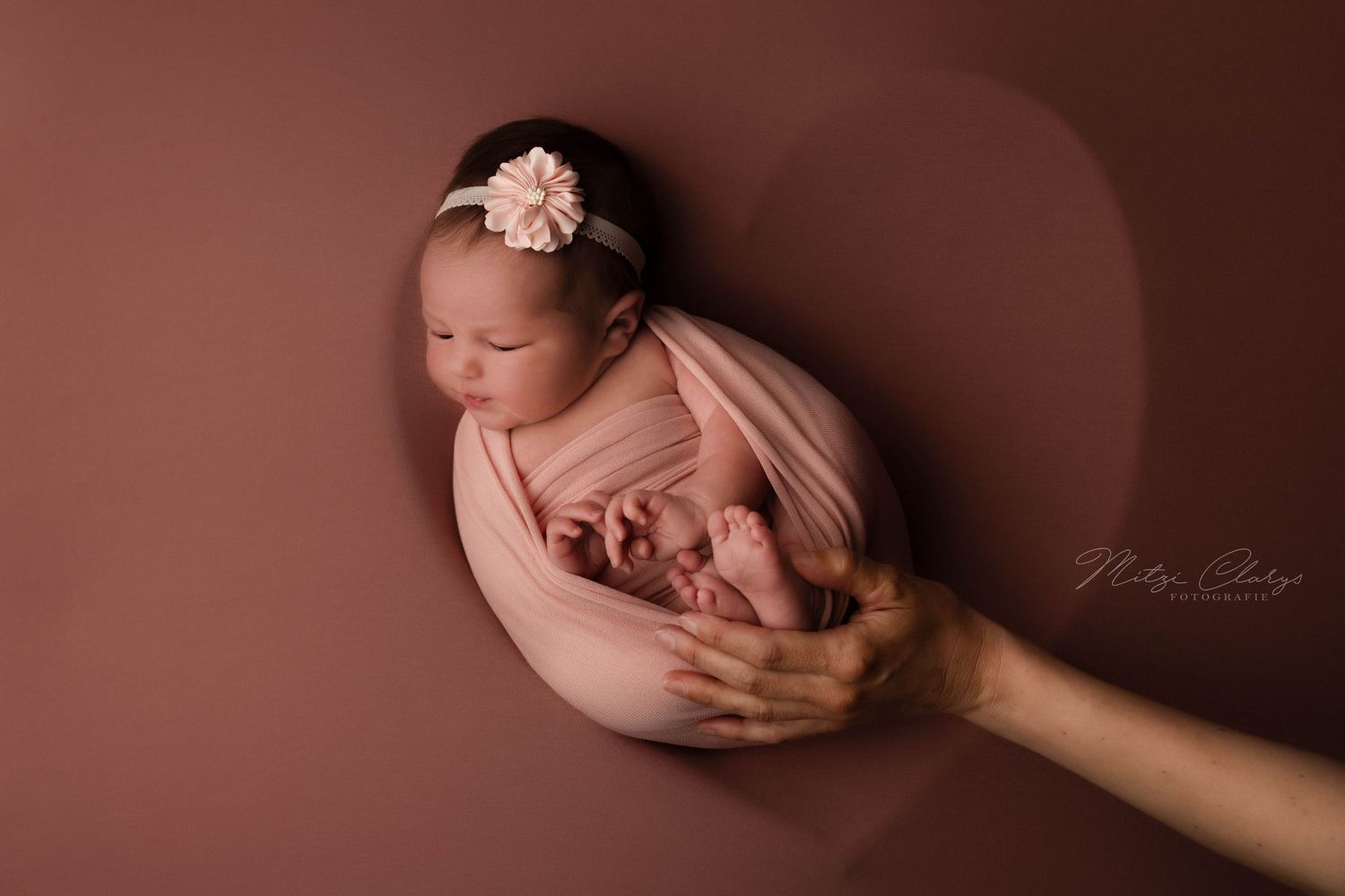 Pasgeboren baby gewikkeld in een zachte wrap in hartvormige schaal tijdens een newbornshoot