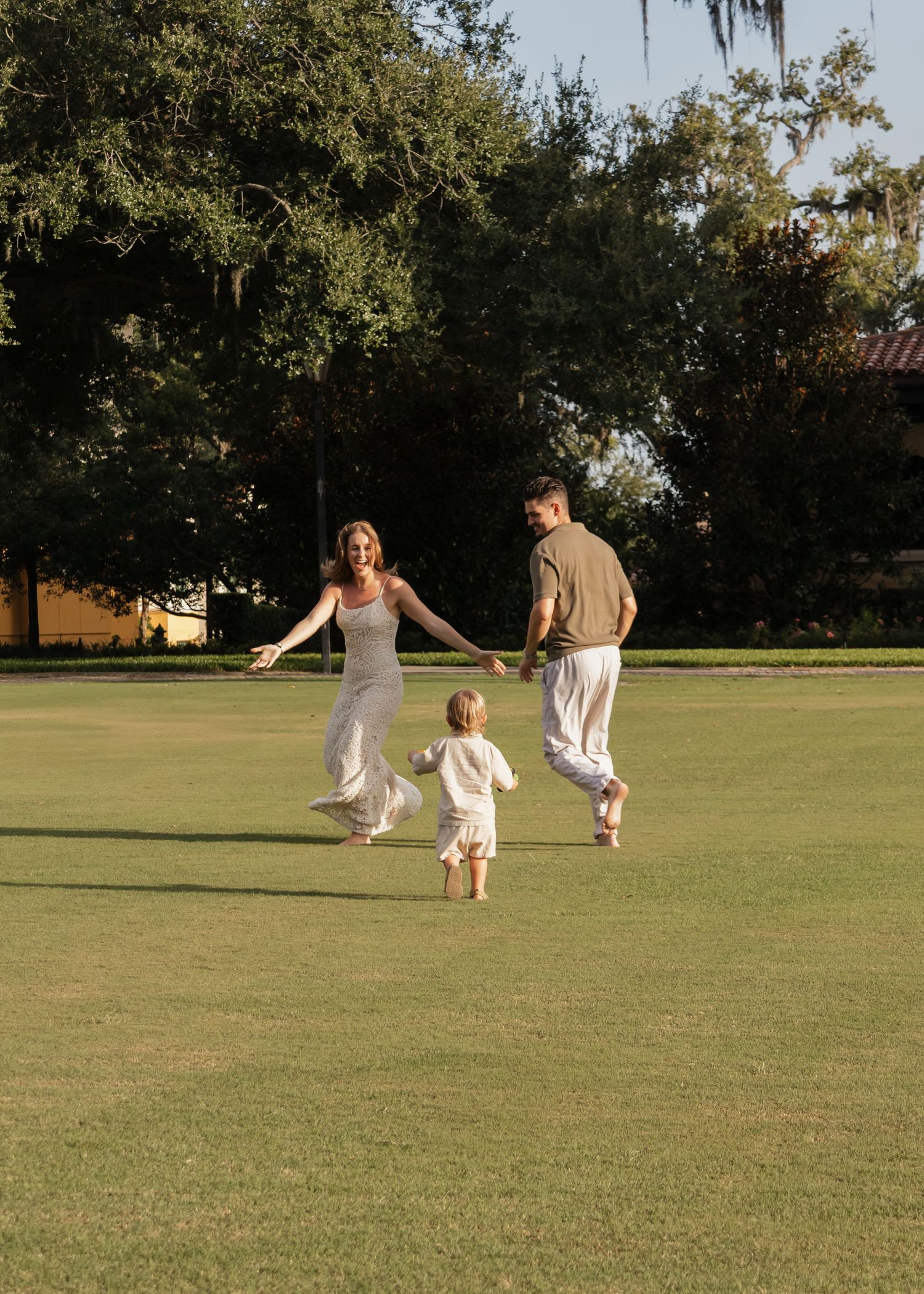 Pregnant woman in pink dress sits with young daughter and man in blue shirt on stone bench outdoors.