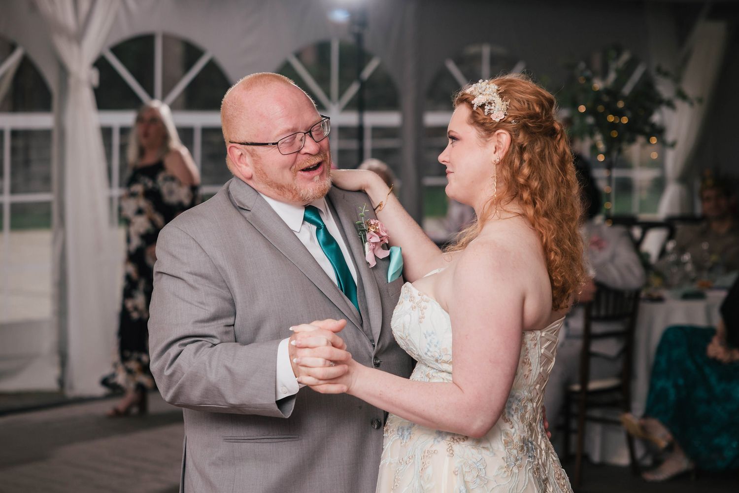 Bride laughing with her father during their father-daughter dance, his hand resting warmly in hers.