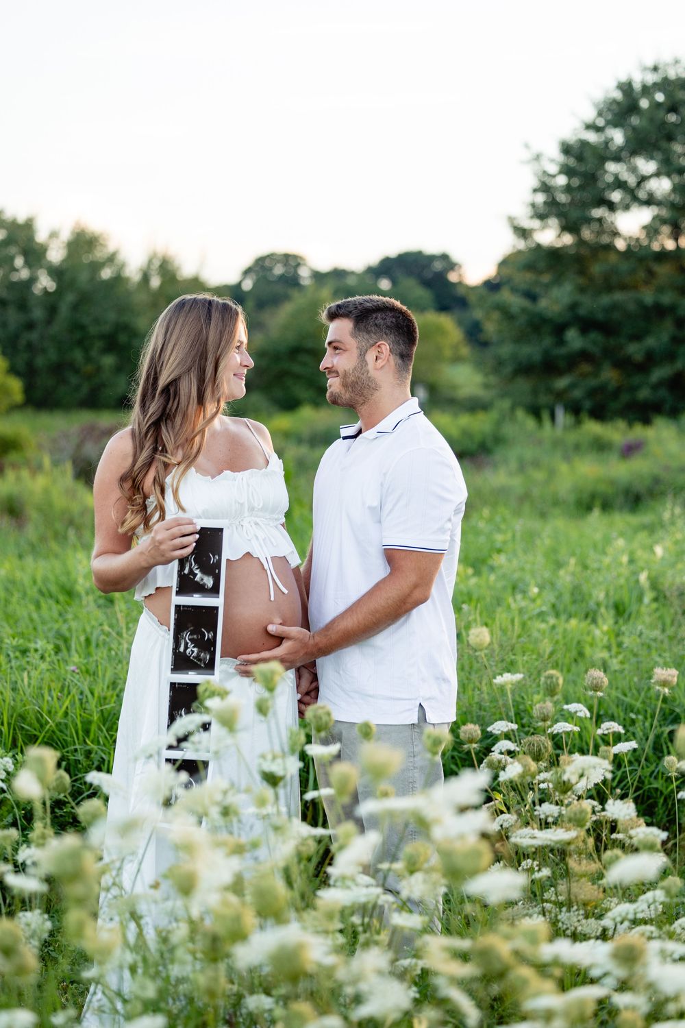 Happy expecting couple holding ultrasound photos in a flower field, celebrating pregnancy outdoors.